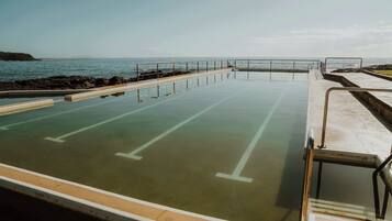 A swimming pool with a view of the ocean, surrounded by a concrete deck and metal railings.