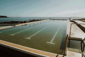 A swimming pool with a view of the ocean, surrounded by a concrete deck and metal railings. - One-Gaea by Tiny Away (Rainbow Flat)