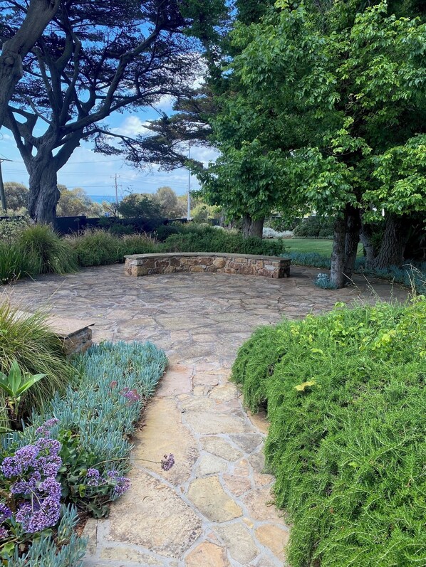 A stone pathway leading to a seating area surrounded by lush greenery and trees.