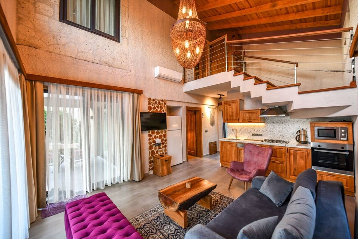 Uma sala de estar ampla com escada, cozinha e uma grande janela com cortinas leves.