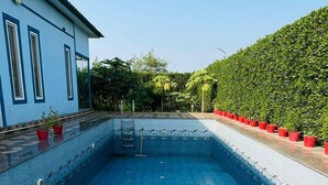 En rektangulär swimmingpool med ett blått kaklat botten, omgiven av en låg mur och en häck.