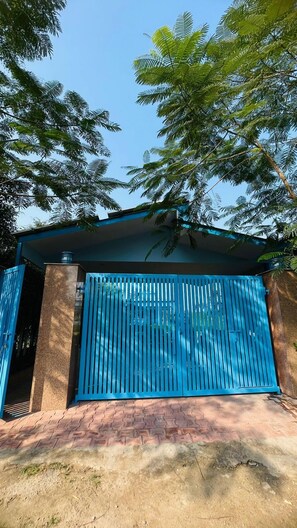 Un edificio con una verja azul, paredes de ladrillo y un árbol sobre él.