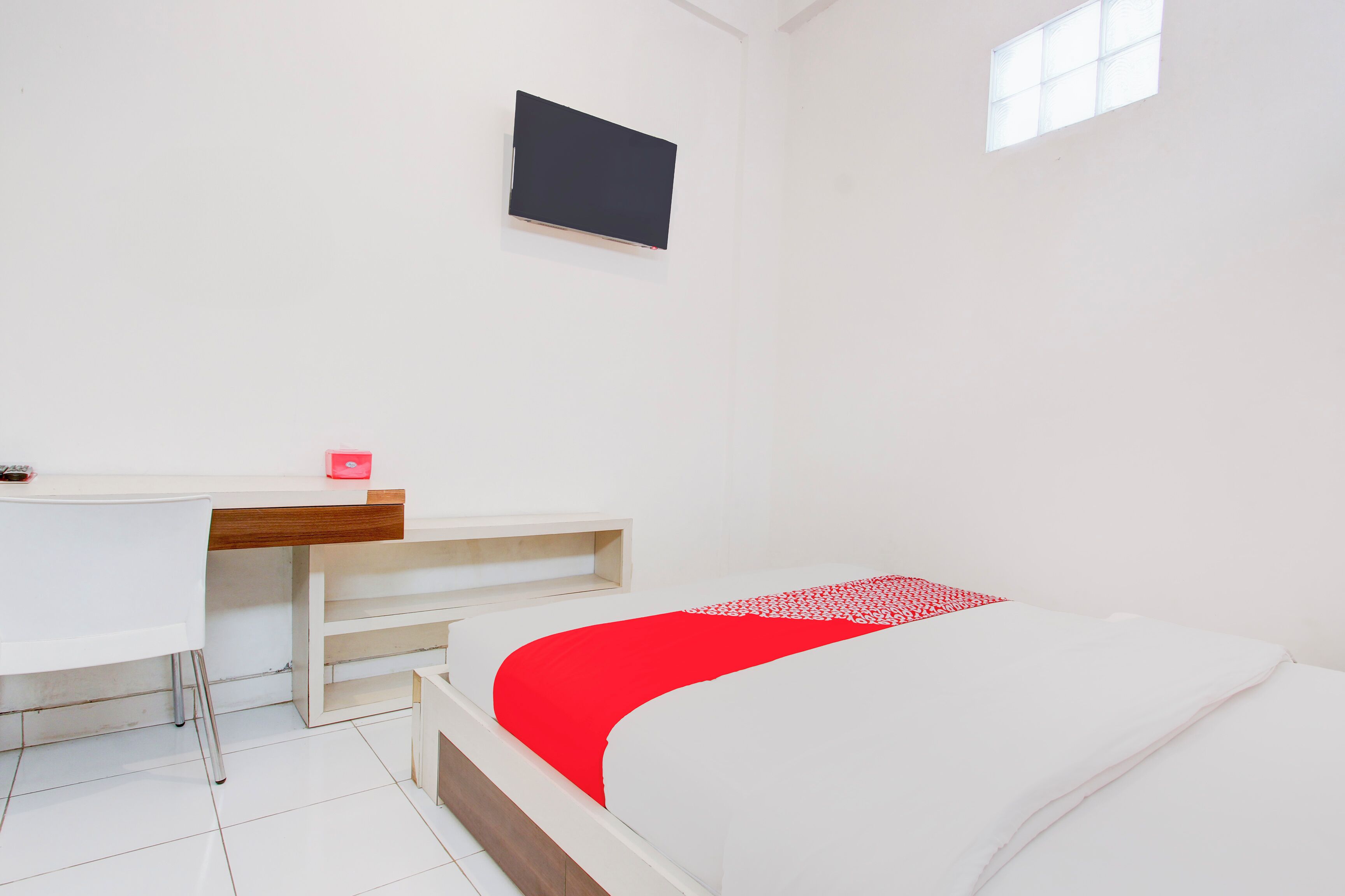 A bedroom with a bed, a desk, and a TV mounted on the wall.