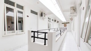 Un couloir propre et blanc, équipé de climatiseurs, muni d’une rambarde et d’une porte portant le numéro 204.