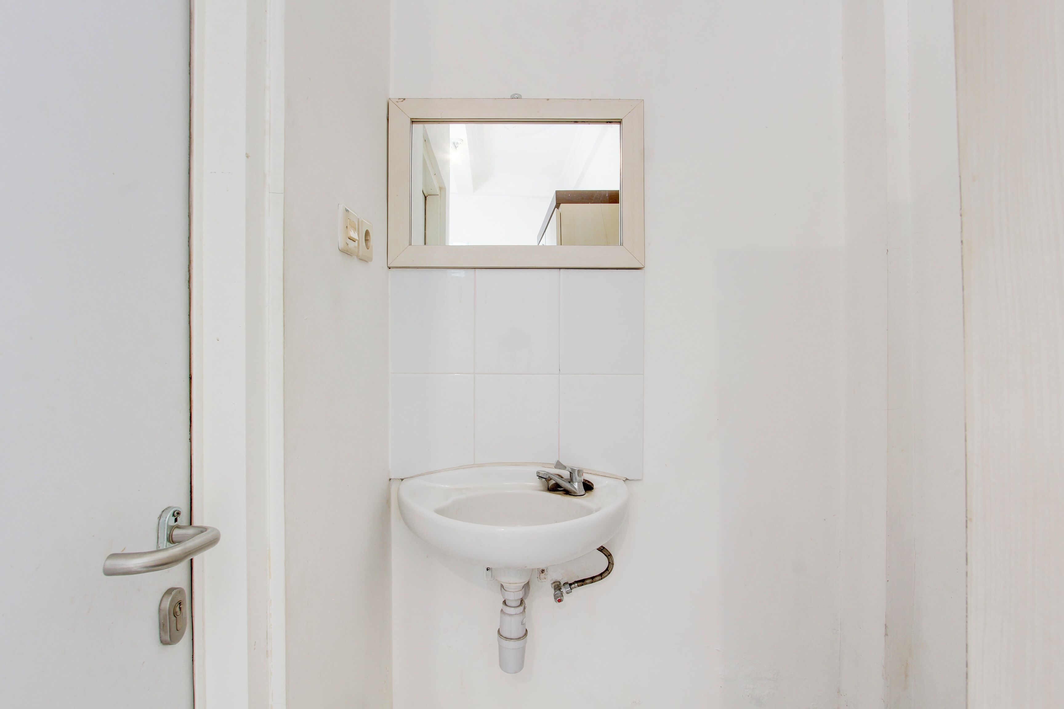 Un baño con un lavamanos blanco, un espejo y una puerta.