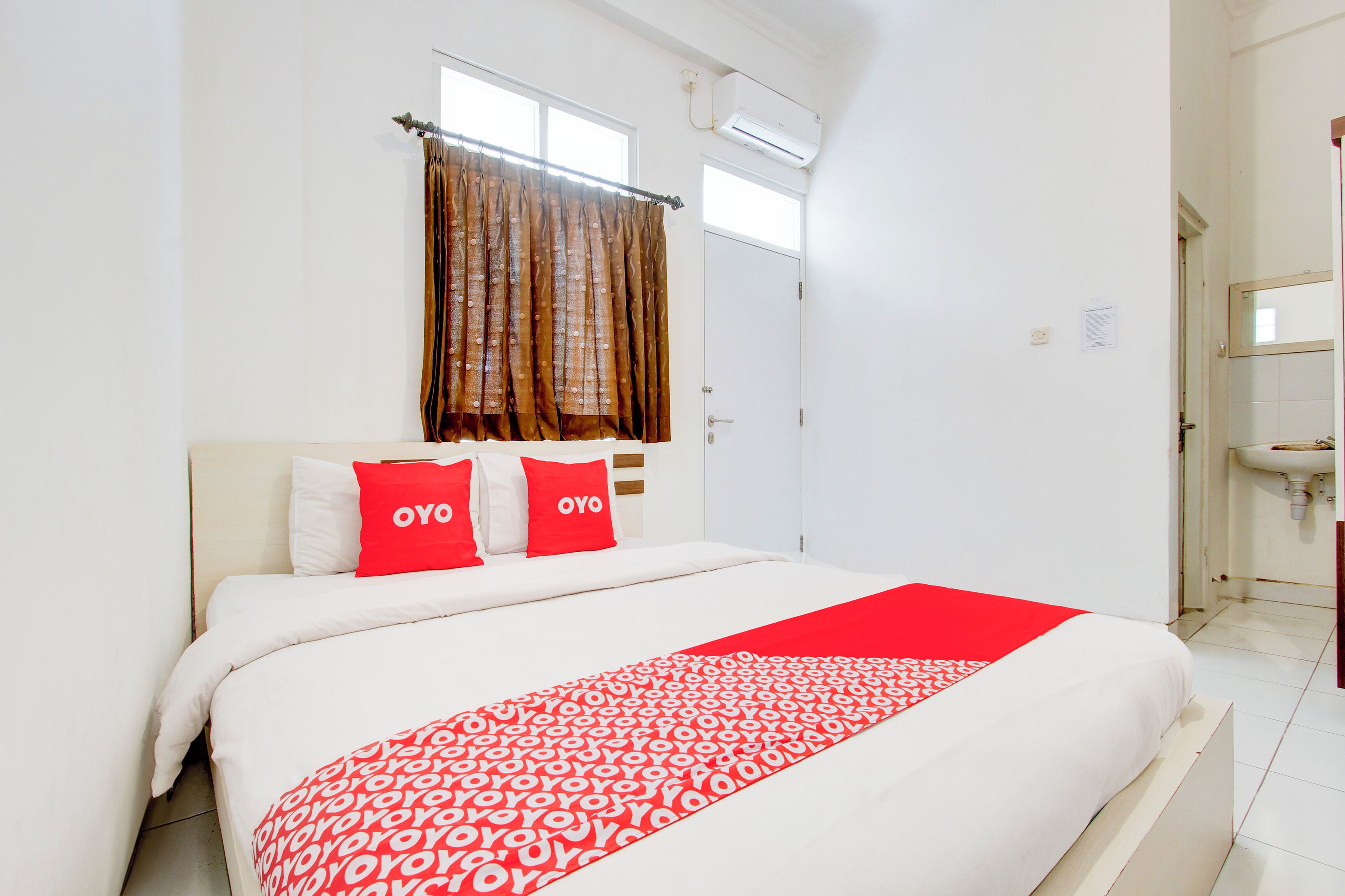 A hotel room with a bed, a window with curtains, a white sink, and a mirror.