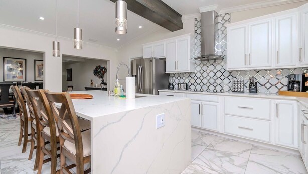 Une cuisine moderne avec des armoires blanches, un îlot en marbre, des luminaires suspendus et une cuisinière intégrée.