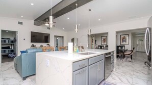 Une cuisine moderne dotée d’un îlot en marbre, de luminaires suspendus et d’un réfrigérateur encastré.
