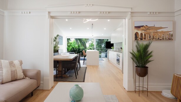 Una cocina moderna con armarios blancos, un comedor con mesa y sillas de madera, y una sala de estar con sofá y mesa de centro.