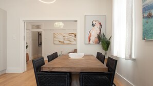 Un comedor con una mesa de madera, sillas de mimbre negro, un centro de mesa con un tazón blanco y obras de arte en las paredes.
