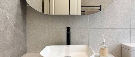Une salle de bain avec un lavabo blanc, un robinet noir, un miroir et un flacon de savon pour les mains de la marque Beach & Natural.