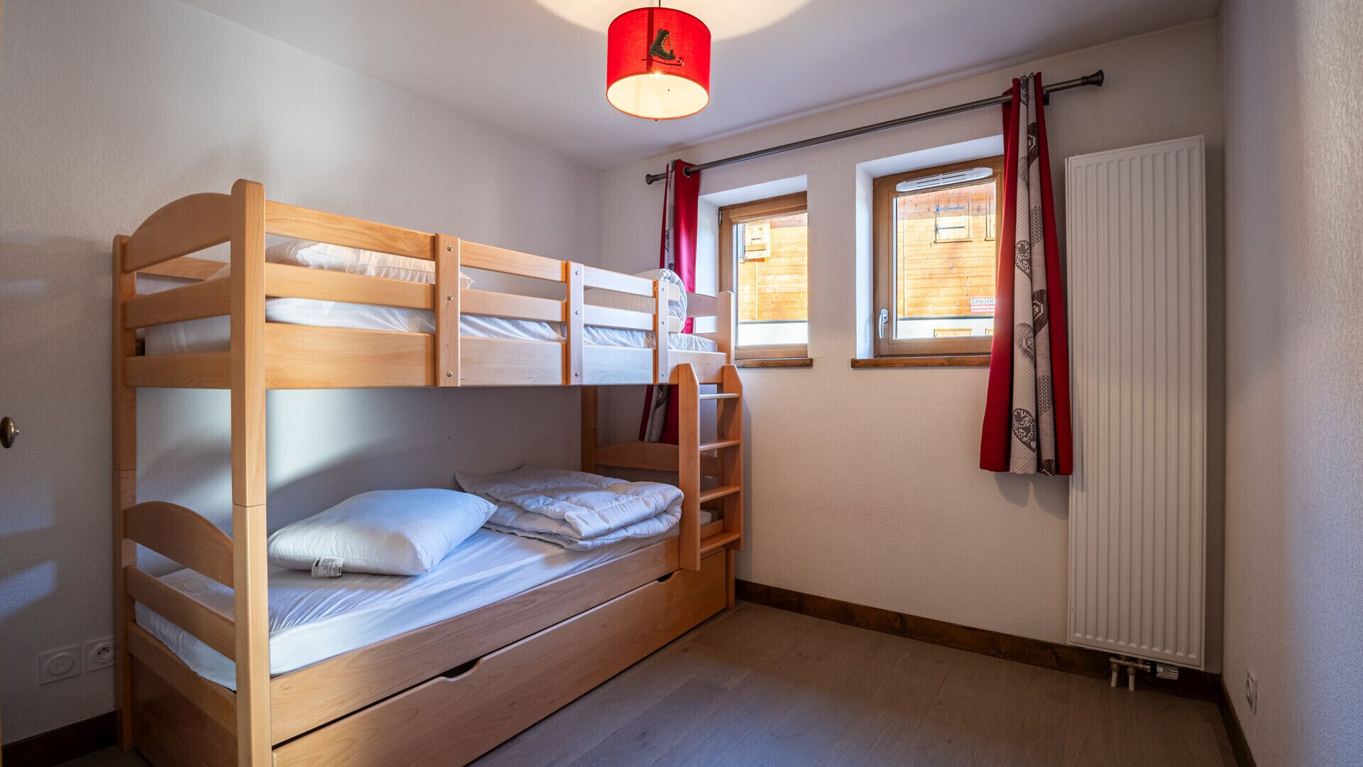 A bunk bed room with a window, curtains, and a radiator.