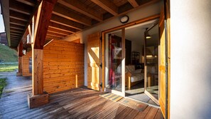 Een houten gevel met een glazen deur die uitkomt in een kamer met een bed en een stoel.