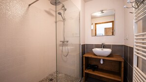 A bathroom with a glass shower enclosure, a white sink, a wooden shelf, and a mirror with a wooden frame. - Beautiful, bright apartment for 6 pers (Morillon)