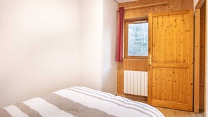 Un dormitorio con una cama, una puerta de madera y una ventana con vistas a árboles.