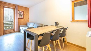 Una habitación acogedora con una mesa de madera, cuatro sillas, un sofá y una ventana con cortinas.