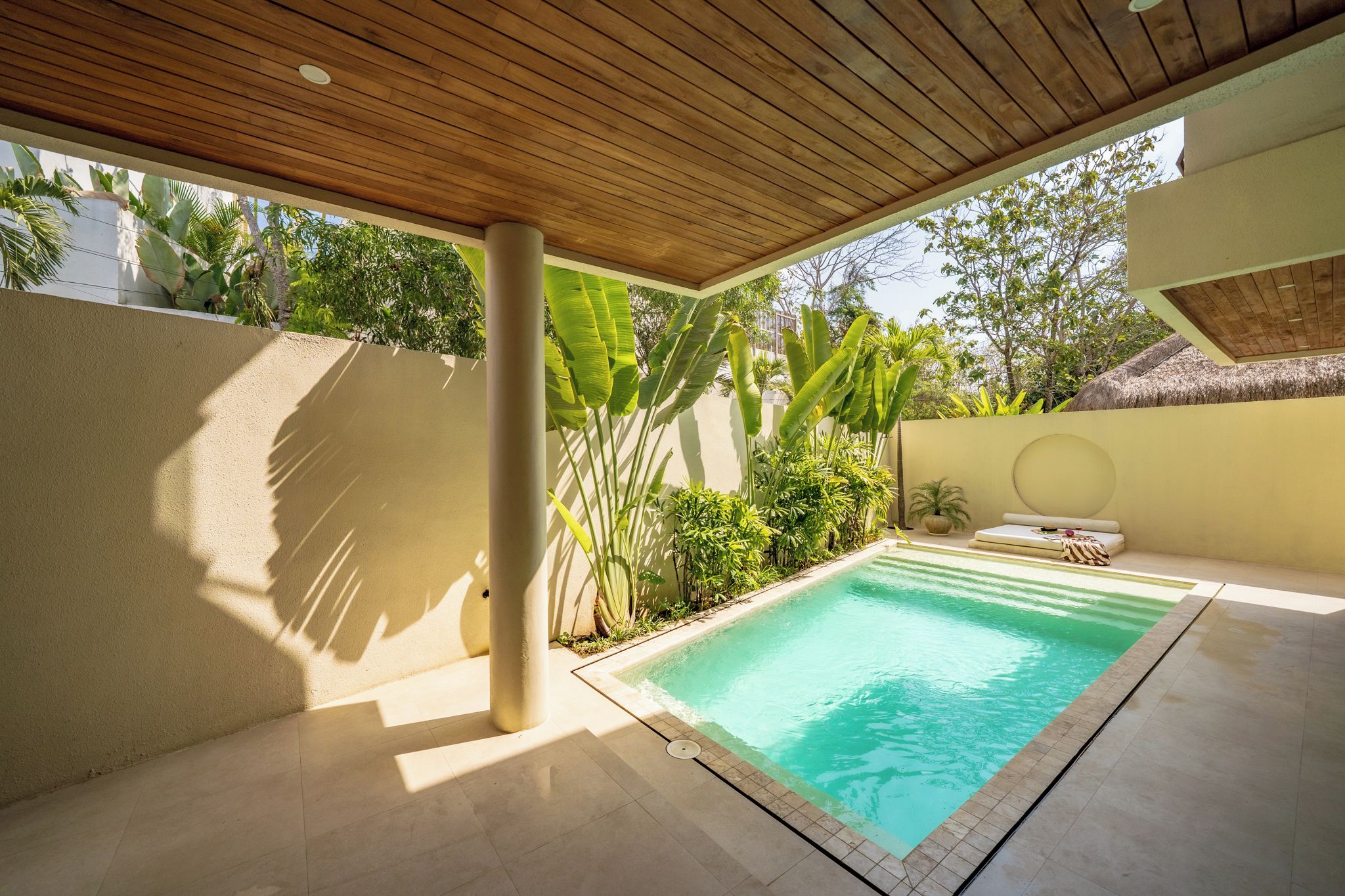 A swimming pool with a wooden ceiling, surrounded by greenery and a tiled floor.