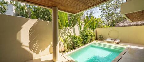 A swimming pool with a wooden ceiling, surrounded by greenery and a tiled floor.