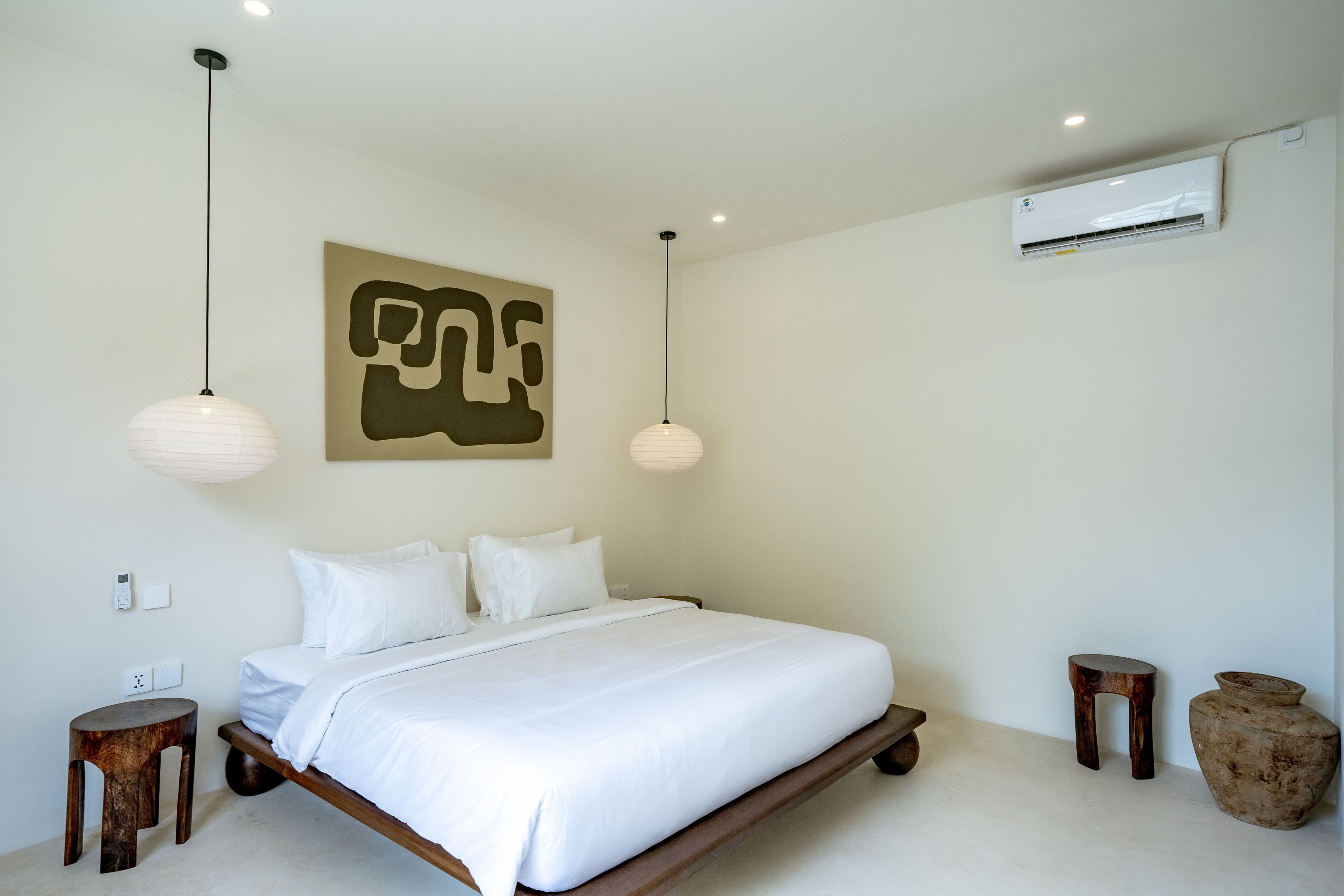 A modern bedroom with a large bed, pendant lights, a wall-mounted air conditioner, and a unique abstract artwork.