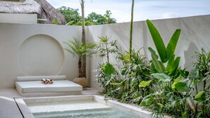 Un área de spa con un jacuzzi, una zona de estar con cojines y exuberante follaje tropical.