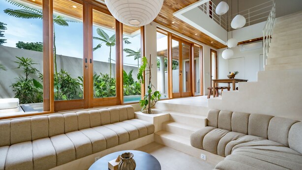 Un interior moderno con un sofá, una mesa de centro y una escalera que lleva a un balcón con plantas.
