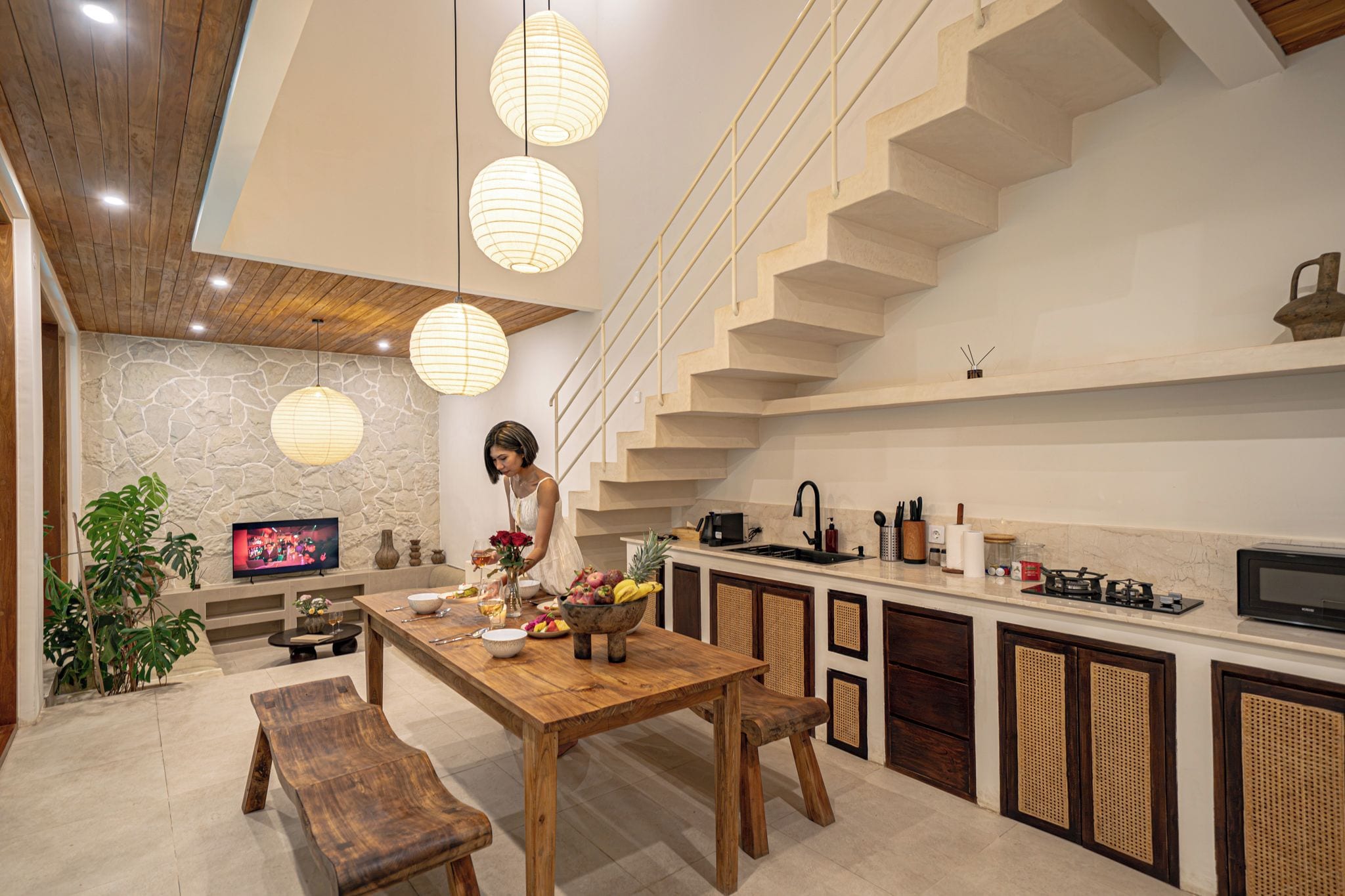 A modern kitchen with a wooden dining table, a built-in stove, and a stone wall.