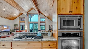 Une cuisine avec des meubles en bois, un plan de travail en granit, une cuisinière, un four à micro-ondes et un four traditionnel.