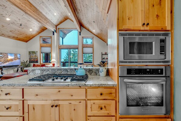 A kitchen with wooden cabinets, a granite countertop, a stove, a microwave, and an oven.