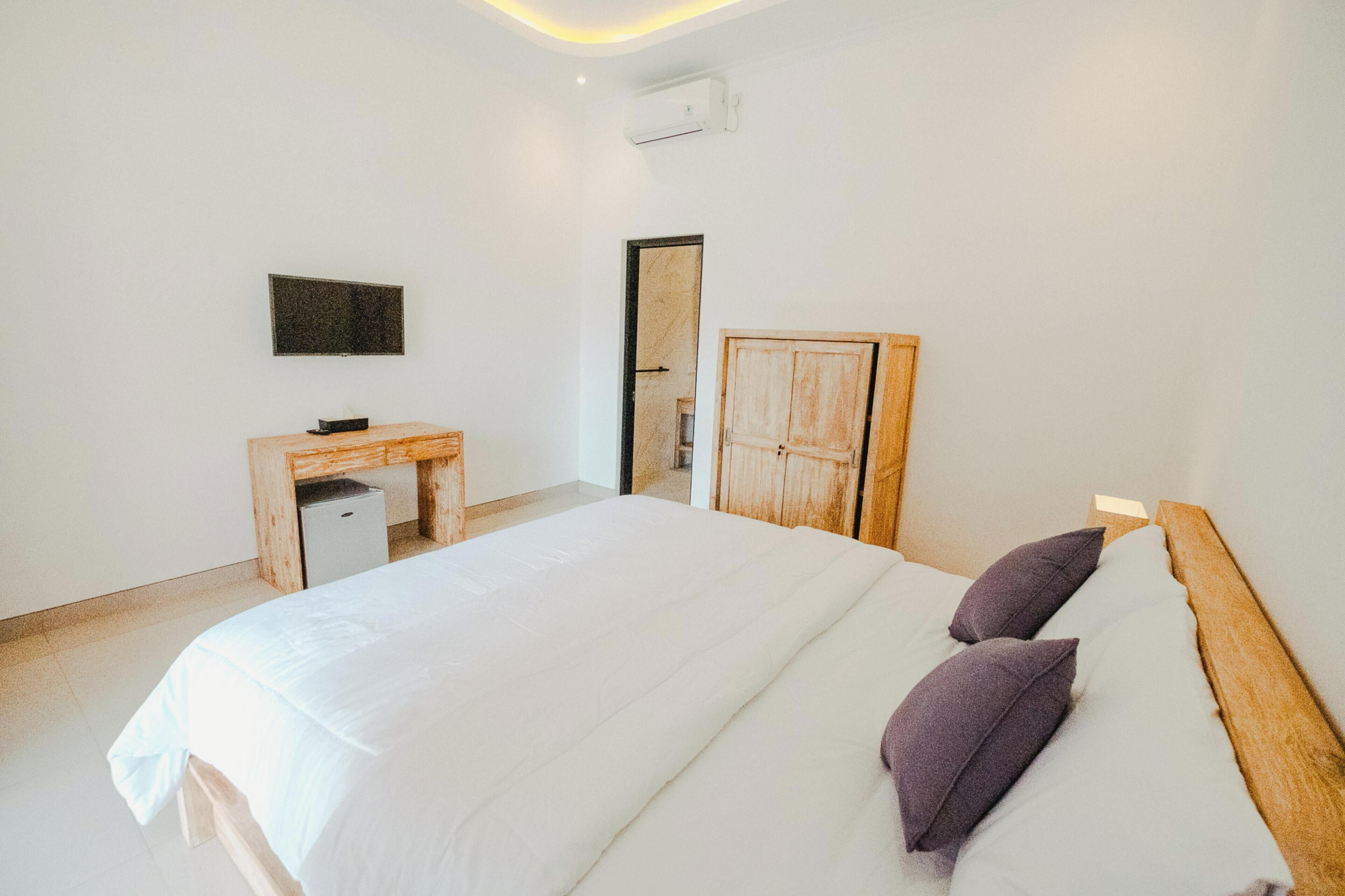 A bedroom with a bed, a wooden headboard, a desk with a chair, a flat-screen TV, and a wardrobe.