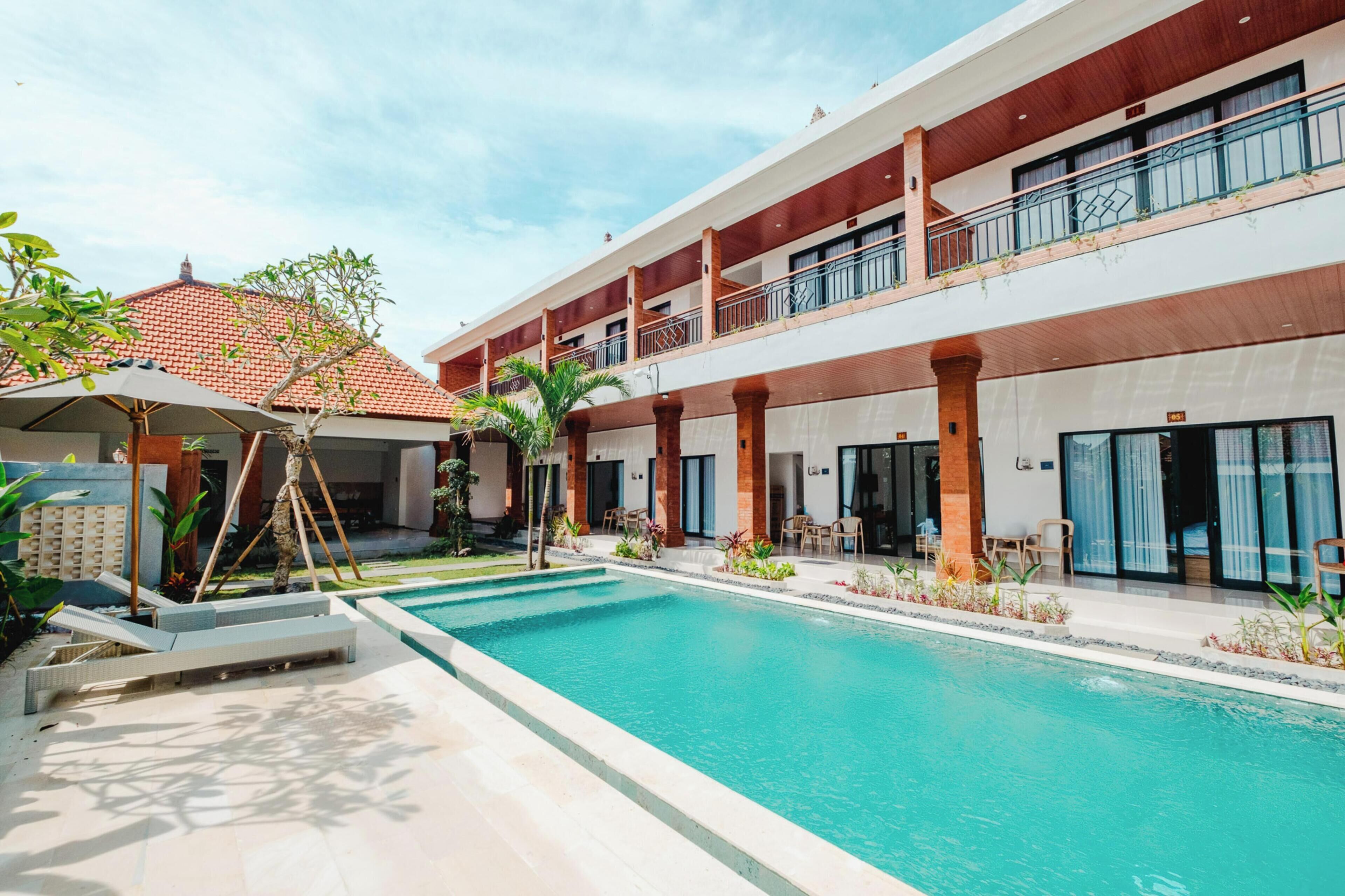 A hotel with a swimming pool, outdoor seating, and a covered area with umbrellas.