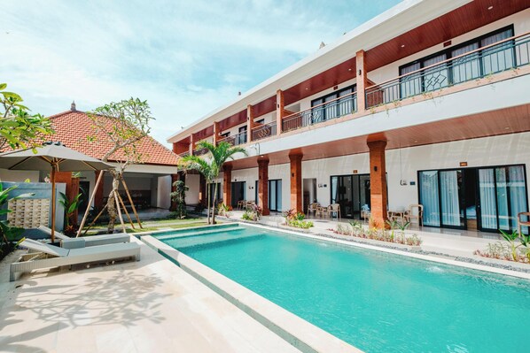Un hotel con piscina, mobiliario exterior y una zona cubierta con sombrillas.