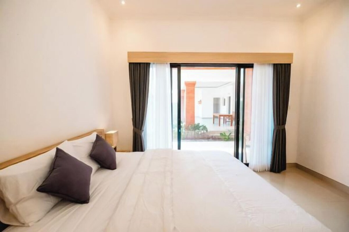 Una habitación de hotel con una cama grande, cabecera de madera y vista a un espacio exterior a través de una puerta de vidrio.