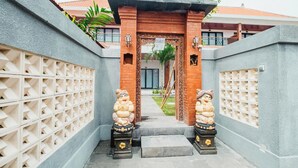 A gated entrance with two statues, a pathway, and a building in the background. - Kubu Dangin Guest House Kerobokan  (Keroboken Kelod)
