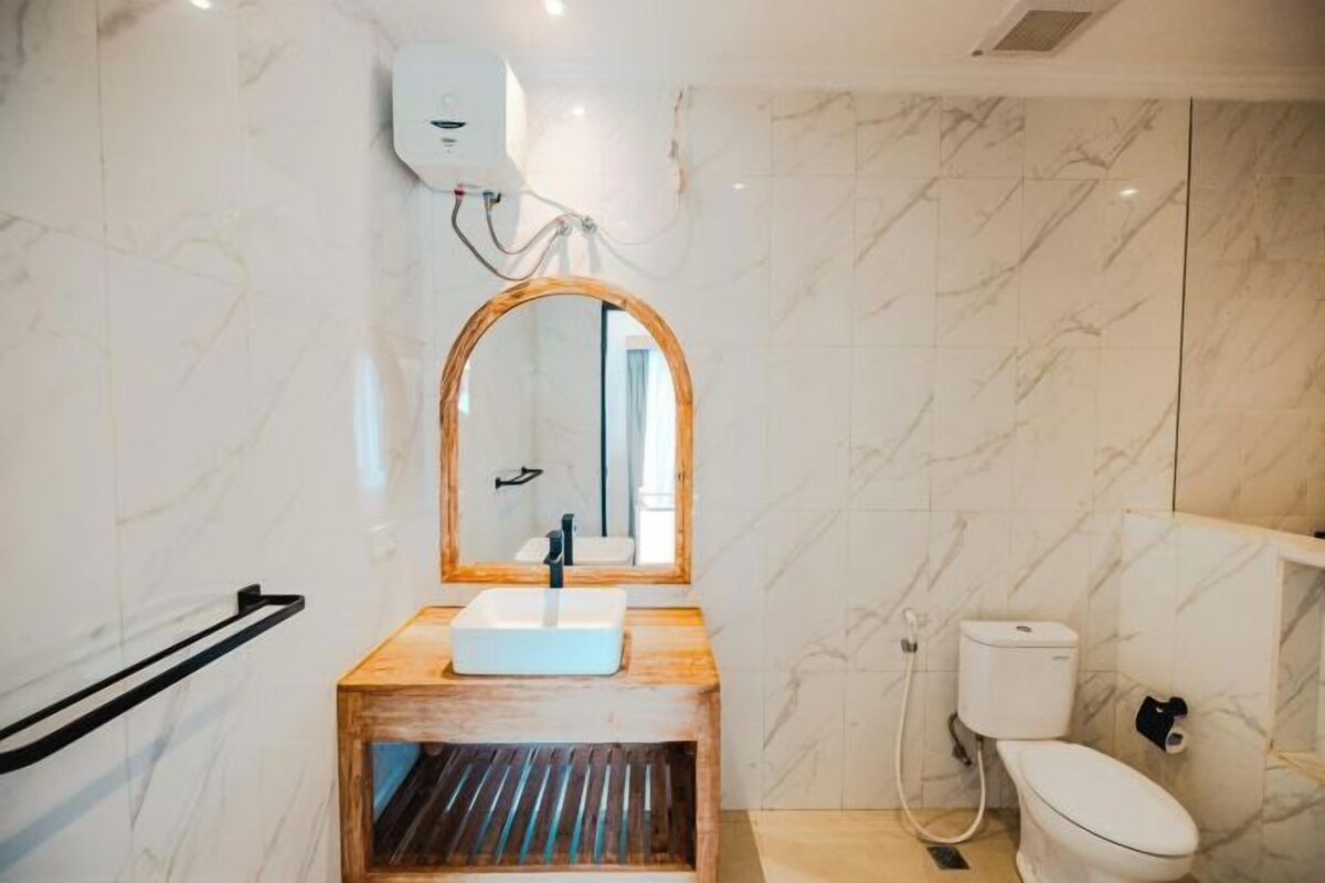 Une salle de bain avec un meuble-lavabo en bois, un lavabo blanc, des toilettes et un miroir avec un cadre en bois.