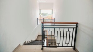 A staircase with a metal railing and a wooden handrail, leading to a bright room with a view of the outside. - Kubu Dangin Guest House Kerobokan  (Keroboken Kelod)