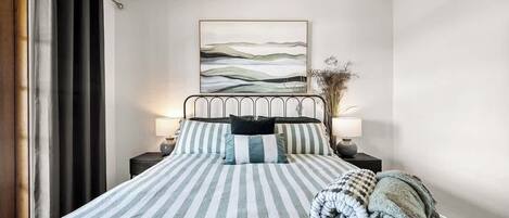 Un lit bien fait, avec une literie à rayures, une lampe de chevet et une œuvre d’art accrochée au mur.
