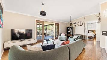 A modern living room with a flat-screen TV, a green sofa, a coffee table, and a dining area with a glass table.