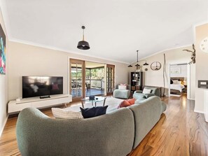 A modern living room with a flat-screen TV, a green sofa, a coffee table, and a dining area with a glass table.