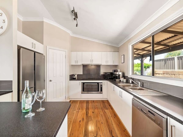 A modern kitchen with a built-in oven, a dishwasher, and a large window overlooking a deck.