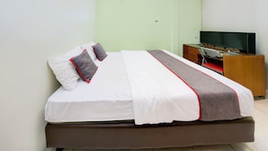 A neatly made bed with white and gray bedding, a wooden nightstand with a television, and a green wall. - Hotel O Tangerang Near Supermall Karawaci  Formerly Bromo 18 (Curug)