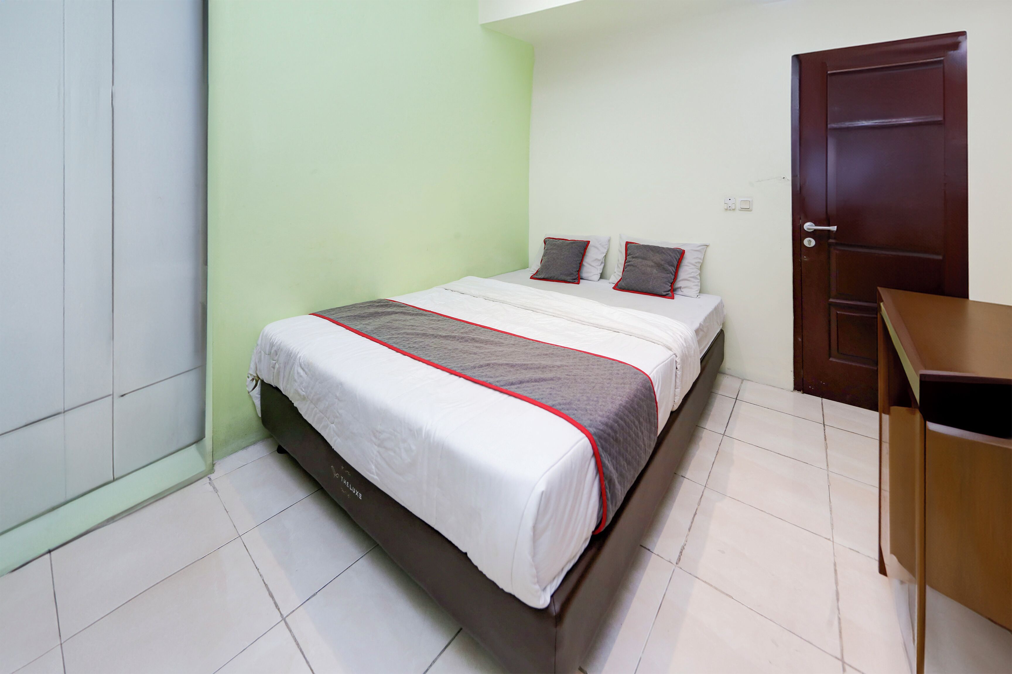 A neatly made bed with a white and gray blanket, a wooden headboard, and a wooden nightstand to the right.