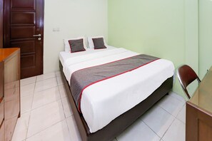 Una cama bien hecha con colcha blanca y gris, dos almohadas y un cabecero de madera.