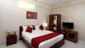 A hotel room with a bed, a TV, a wardrobe, and two framed pictures on the wall. - Coral Tree (Bengaluru)