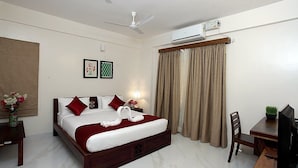 A hotel room with a bed, a desk, a chair, a TV, an air conditioner, a ceiling fan, and curtains. - Coral Tree (Bengaluru)