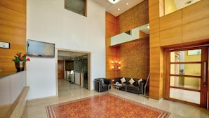 A lobby with a patterned carpet, a sofa, a TV, and a reception desk. - Coral Tree (Bengaluru)
