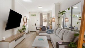 A modern living room with a flat-screen TV, a sofa, a coffee table, and a dining area with a table and chairs.