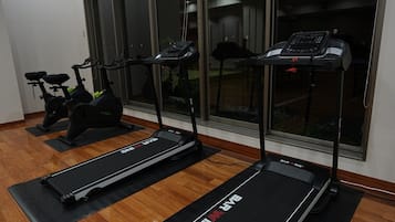 Three stationary bikes and two treadmills in a room with wooden flooring and large windows.