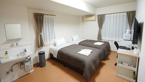 Ett hotellrum med två sängar, ett skrivbord med en dator, ett handfat och en luftkonditioneringsanläggning.