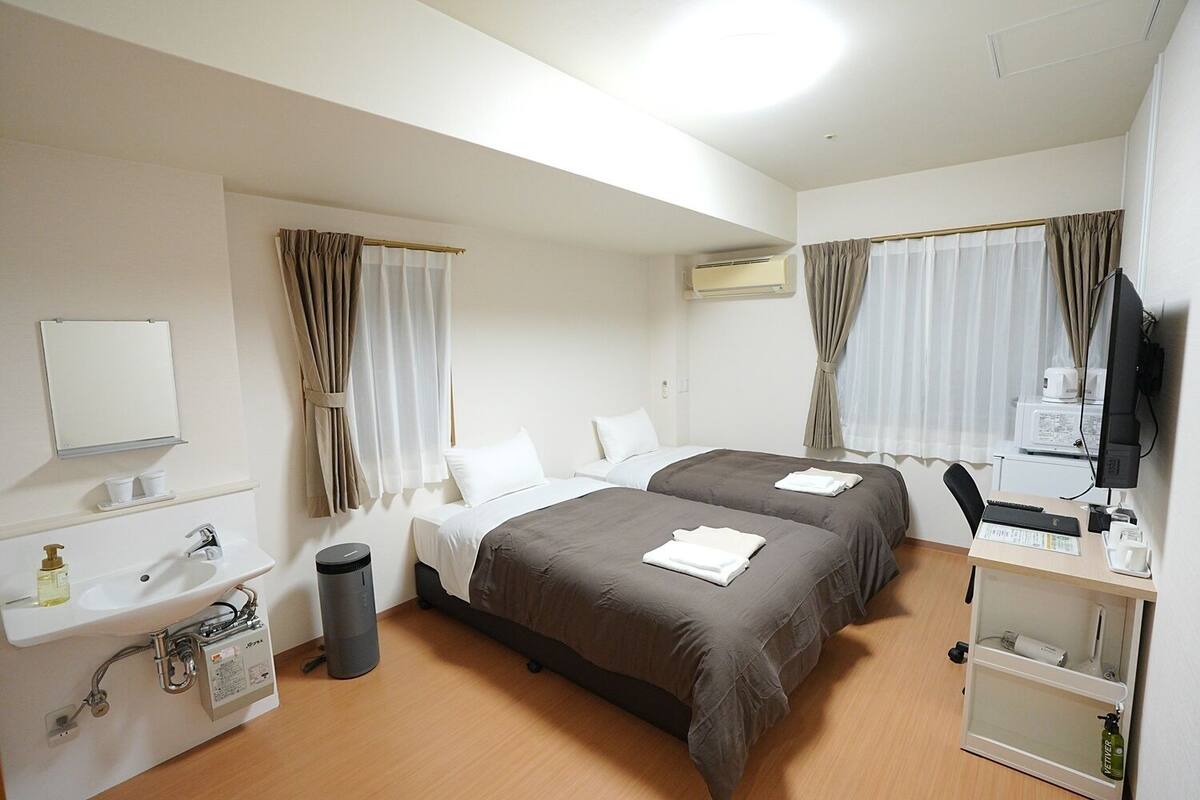 Een hotelkamer met twee bedden, een bureau met een computer, een wastafel en een airconditioning.