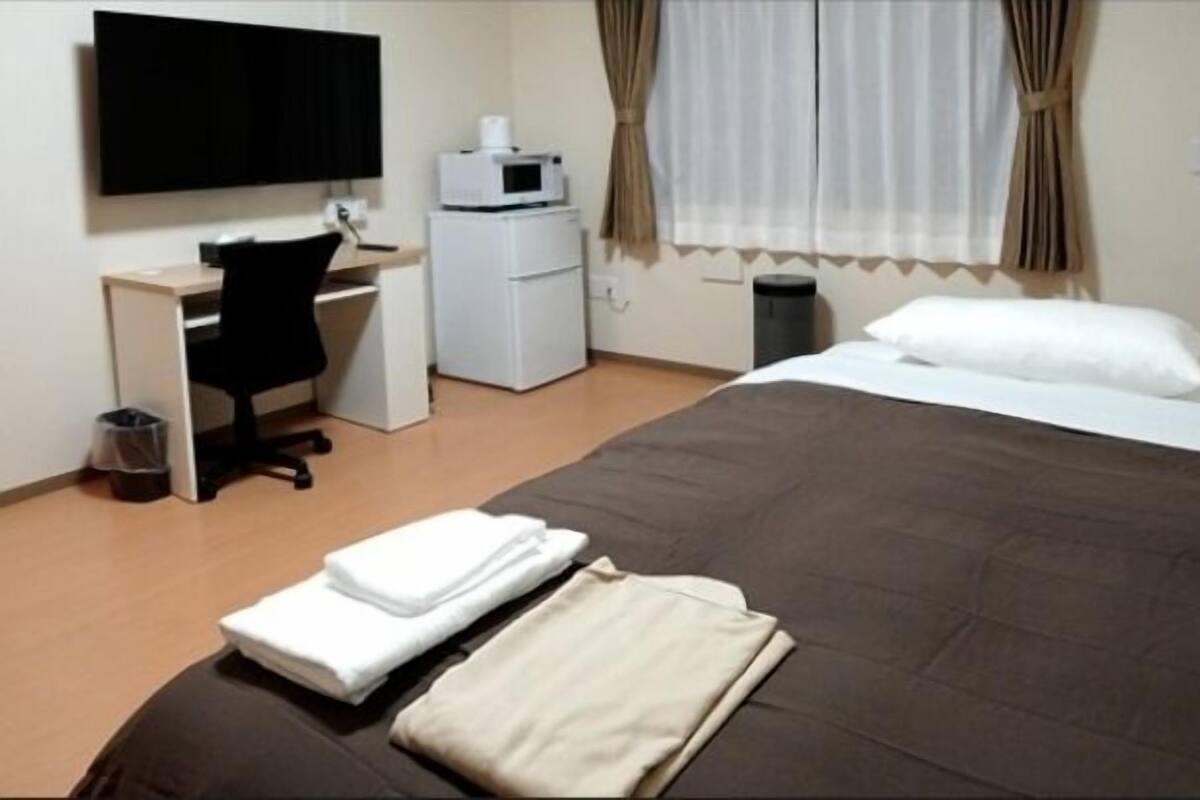 Een hotelkamer met een bed, een bureau, een stoel, een televisie, een magnetron en een prullenbak.